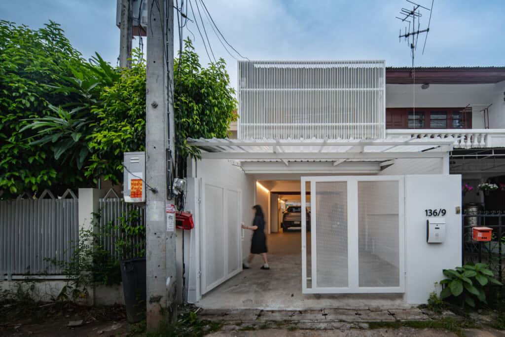 เฟอร์นิเจอร์บ้านหลังสีขาวพร้อมประตูรั้วอัตโนมัติและรถจอดในโรงจอดรถ สร้างจากโครงการรีโนเวทอาคารตึกแถวเป็น Airbnb.